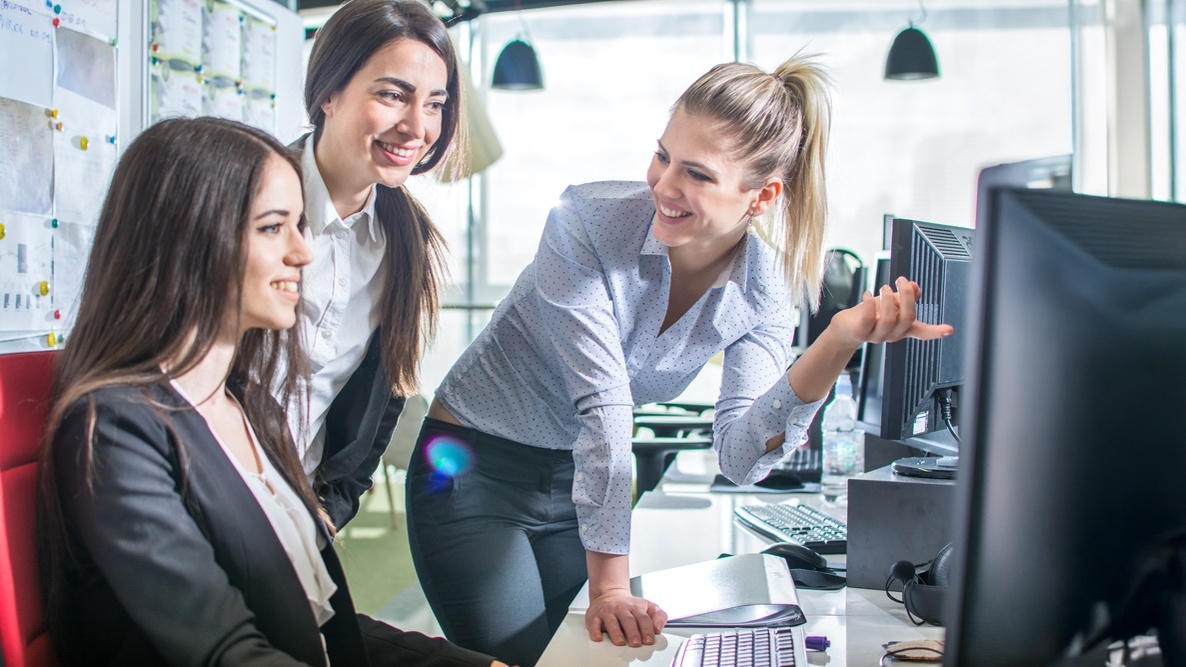 Trois collègues souriantes découvrent Coach Prospecting Sales à l'écran dans un bureau lumineux